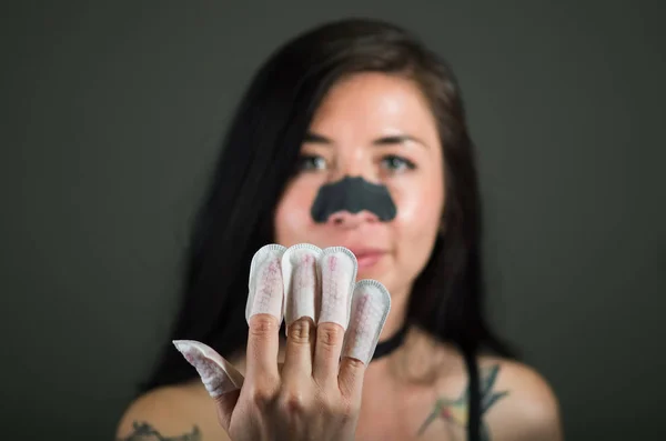 Nahaufnahme einer jungen Frau mit Nagelschutz in den Nägeln und Nasenmaske, um die Haut von schwarzen Flecken zu reinigen, vor schwarzem Hintergrund — Stockfoto