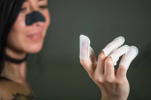 Zbliżenie na młoda kobieta sobie paznokcie protector w jej paznokcie i maska nos do czyszczenia skóry z czarne plamy na czarnym tle — Zdjęcie stockowe