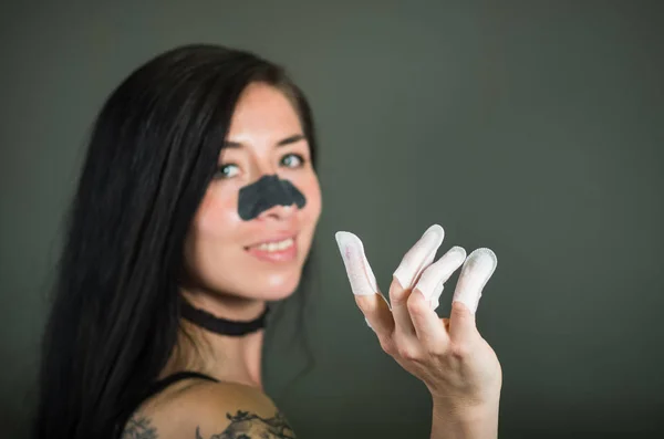 Nahaufnahme einer jungen Frau mit Nagelschutz in den Nägeln und Nasenmaske, um die Haut von schwarzen Flecken zu reinigen, vor schwarzem Hintergrund — Stockfoto