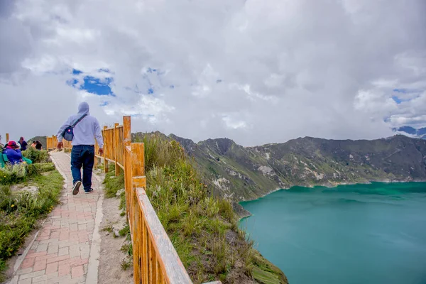 Jovem caminhando na fronteira com um corrimão de madeira segurity, com uma bela vista da caldeira lago Quilotoa. Quilotoa é o vulcão ocidental na cordilheira dos Andes e está localizado na região andina de — Fotografia de Stock