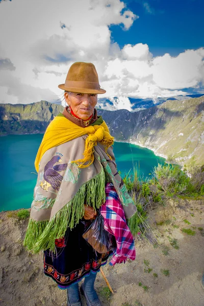 QUITO, ECUADOR - NOVEMBRO, 25 2016: Mulher idosa indígena não identificada vestindo uma roupa típica andina em frente ao lago Quilotoa com uma bela cor magenta da caldeira Quilotoa. Quilotoa é — Fotografia de Stock