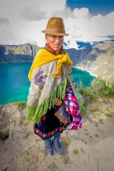 QUITO, ECUADOR - NOVEMBER, 25 2016: Unidentified indigenous old woman wearing a typical andean clothes in front of the Quilotoa lake with a beautiful magenta color of the Quilotoa caldera. Quilotoa is — Stock Photo, Image