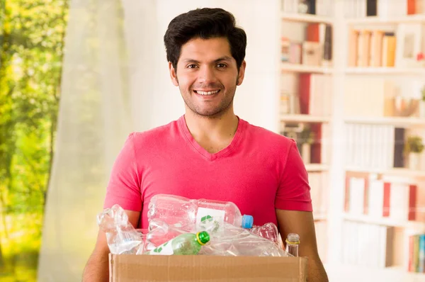 Joven sonriente llevando una caja de cartón llena de plástico, llevando una camiseta rosa, reciclando y protegiendo al mundo del concepto de calentamiento global —  Fotos de Stock