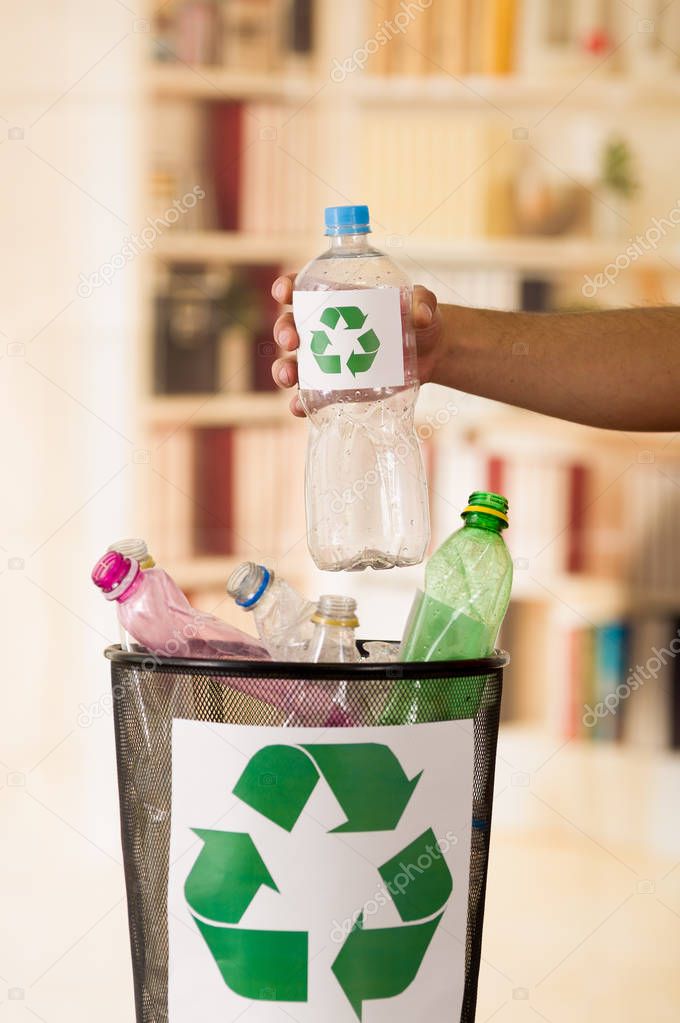 Close up of a hand putting a plastic bottle inside of a small black garbage collector full of plastic, with a recycling sign printed in front, recycle and safe the world from global warming concept