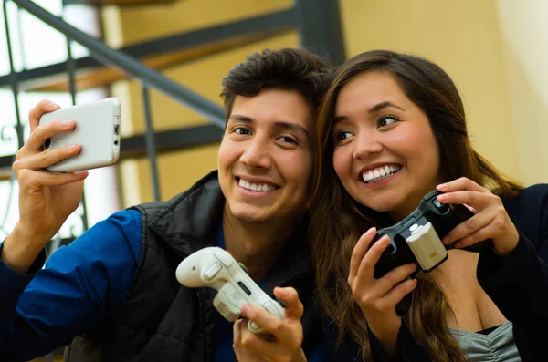 Beau couple jouant à des jeux vidéo sur le canapé tenant dans leurs mains une manette de jeu pendant qu'il prend un selfie, concept de divertissement à la maison, jeux vidéo — Photo