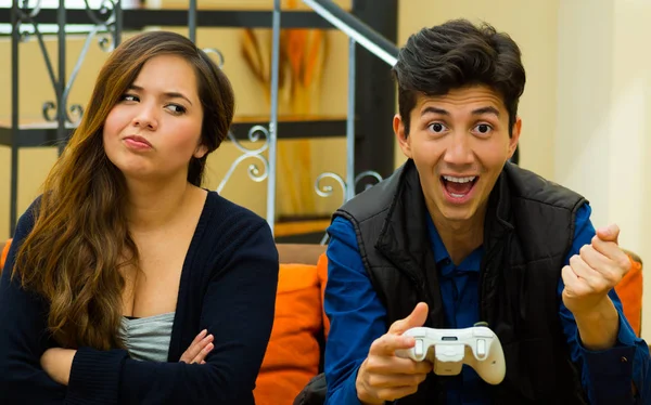 Feliz joven jugando videojuegos en el sofá mientras su novia está aburrida, concepto de entretenimiento en el hogar, videojuegos — Foto de Stock