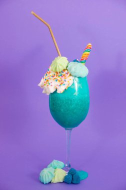 Lezzetli ev yapımı aşırı milkshake bir süt köpüğü ve gökkuşağı şeker mor bir arka planda plastik pipet ile üst üzerinde drajelik ile