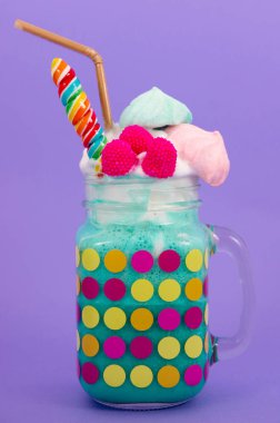 Lezzetli ev yapımı aşırı milkshake bir süt köpük üzerinde blackberry şeker ve gökkuşağı şeker üstüne bir kavanoza mor bir arka planda plastik pipet ile