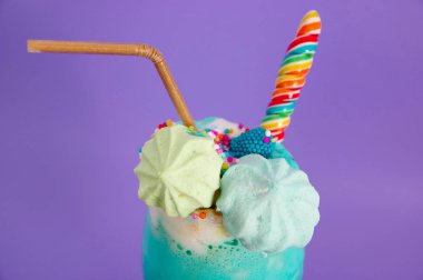 Süt köpüğü ve gökkuşağı şeker mor bir arka planda plastik pipet ile üst üzerinde drajelik ile lezzetli ev yapımı aşırı milkshake, yakın çekim