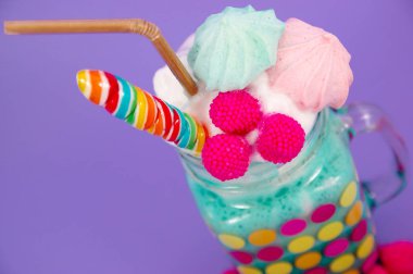 Lezzetli ev yapımı aşırı milkshake bir süt köpük üzerinde blackberry şeker ve gökkuşağı şeker üstüne bir kavanoza mor bir arka planda plastik pipet ile