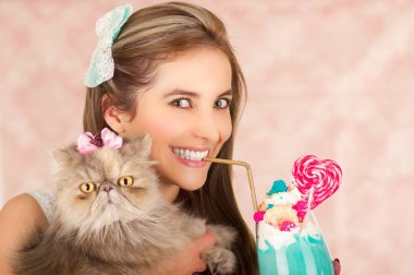 Gülümseyen genç güzel kadın lezzetli mavi milk shake bir kalp şeker ile studio moda ile plastik bir süt saman köpük üstte, pembe bir arka planda kedisini sarılma