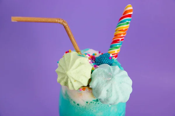 Närbild på en utsökt hemlagad extrema milkshake med dragéer över ett mjölkskum och en regnbåge godis på toppen med en plast halm i en lila bakgrund — Stockfoto
