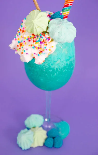 Läcker hemmagjord extrema milkshake med dragéer över ett mjölkskum och en regnbåge godis på toppen med en plast halm i en lila bakgrund — Stockfoto