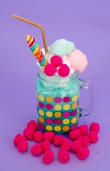 Heerlijke zelfgemaakte extreme milkshake in een pot met een blackberry snoep over een melk schuim en een snoepje van de regenboog op de top met een plastic stro, met een rode blackberry snoep in de basis van de pot, in een paars — Stockfoto