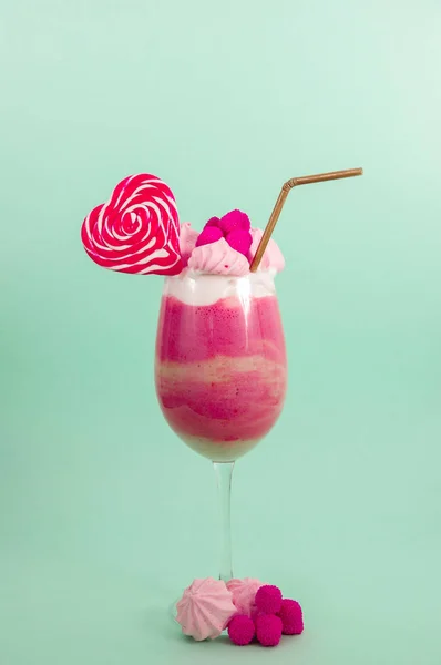 Delicious homemade extreme milkshake of strawberry with milk foam with a plastic straw and a pink blackberry candy with a heart candy on top, in a soft blue background — Stock Photo, Image