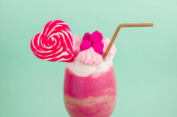 Närbild på en utsökt hemlagad extrema milkshake av jordgubbar med mjölkskum med en plast som halm och en rosa blackberry godis med en hjärtat godis på toppen, i en mjuk blå bakgrund — Stockfoto