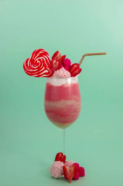 Delicious homemade extreme milkshake of strawberry with milk foam with a plastic straw and a pink blackberry candy with a heart candy on top, in a soft blue background — Stock Photo, Image