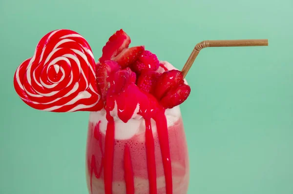 Délicieux milkshake maison extrême de fraise avec mousse de lait avec une paille en plastique et un bonbon à la mûre rose avec un bonbon au cœur sur le dessus, dans un fond bleu doux — Photo