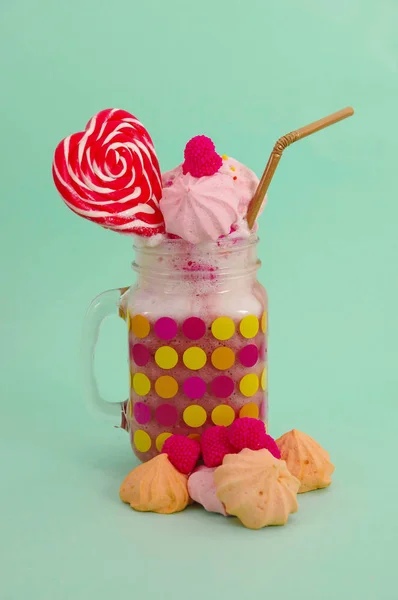 Läcker hemmagjord extrema milkshake av jordgubb i en burk, med en blackberry godis över en mjölk skum med en plast som halm och en rosa blackberry godis med en hjärtat godis på toppen, i en mjuk blå — Stockfoto