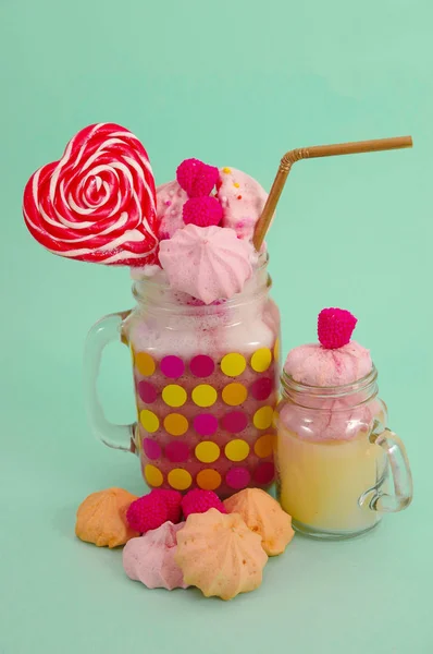Läckra extrema milkshake av jordgubb i en burk, med en blackberry godis över ett mjölkskum med en plast som halm och en rosa blackberry godis med en hjärtat godis på toppen, i en mjuk blå bakgrund — Stockfoto
