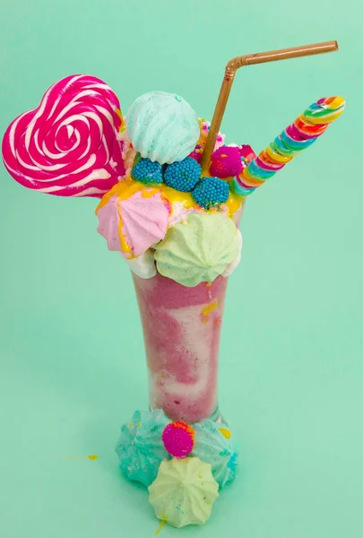 Délicieux milkshake extrême de fraise avec des dragees et un bonbon à la mûre sur une mousse de lait avec une paille en plastique et un bonbon au cœur sur le dessus, dans un fond bleu doux — Photo