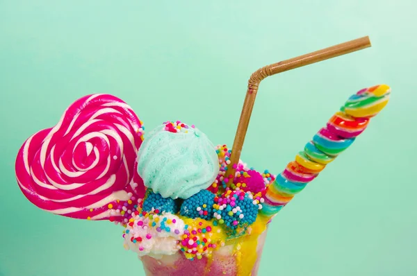 Dekat milkshake ekstrim lezat stroberi dengan dragees dan permen blackberry di atas busa susu dengan sedotan plastik dan permen jantung di atas, di latar belakang biru lembut — Stok Foto