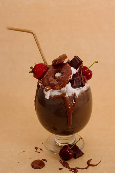 Chocolate indulgent extreme milkshake with brownie cake, strawberries, cherries, and a plastic straw with milk foam on top in a soft brown background — Stock Photo, Image