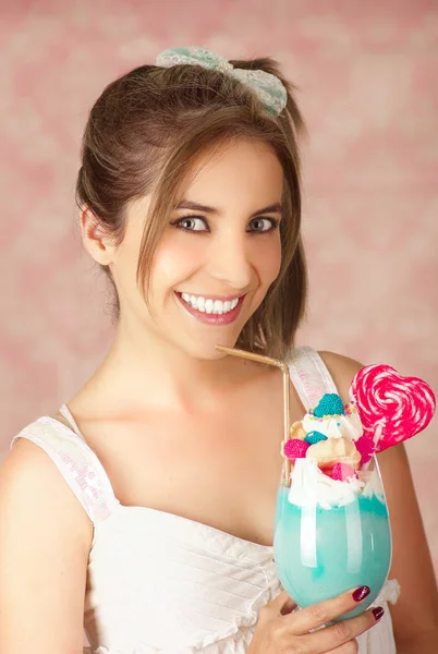 Primo piano di una giovane donna sorridente che tiene in mano un gustoso frullato di latte blu, trucco, vestiti alla moda, moda da studio in uno sfondo rosa — Foto Stock