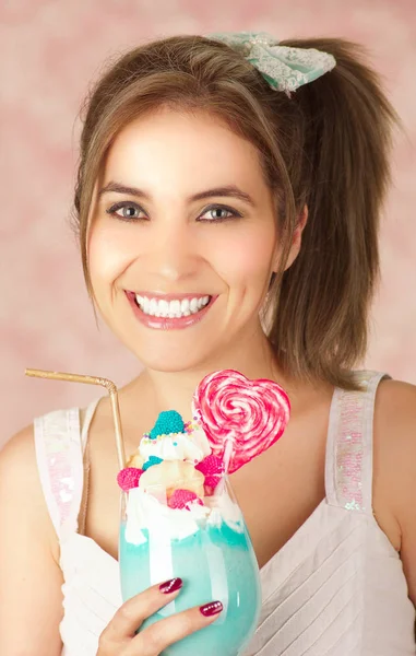 Primo piano di una giovane donna sorridente che tiene in mano un gustoso frullato di latte blu, trucco, vestiti alla moda, moda da studio in uno sfondo rosa — Foto Stock