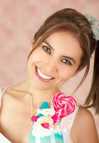 Primo piano di una giovane donna sorridente che tiene in mano un gustoso frullato di latte blu, trucco, vestiti alla moda, moda da studio in uno sfondo rosa — Foto Stock
