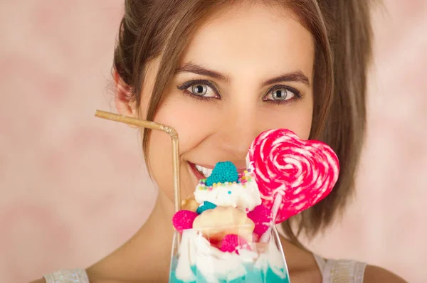Primo piano di bella donna carina in possesso di un gustoso frullato di latte blu con un cuore di caramelle sulla parte superiore, vestiti alla moda, studio di moda in uno sfondo rosa — Foto Stock