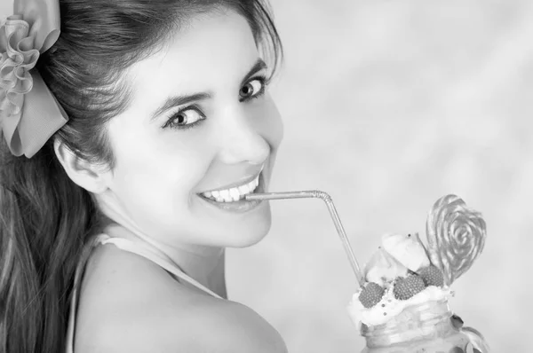 Mulher sorridente, usando uma mala rosa, segurando um saboroso batido de leite azul em um frasco, com um doce de coração, palha de plástico em uma espuma de leite em cima, em um fundo rosa, em efeito preto e branco — Fotografia de Stock