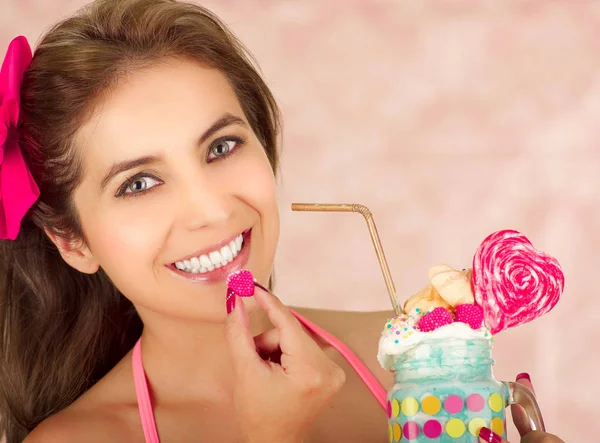 Indoor portrait of pretty cute woman with blackberry in her hand ready eat and holding with her other hand a tasty milk shake in a jar, in a pink background — Stock Photo, Image