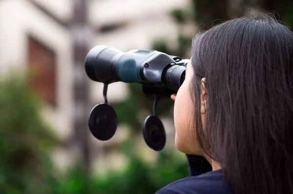 Mujer joven acechando con unos prismáticos negros en un fondo de la ciudad — Foto de Stock