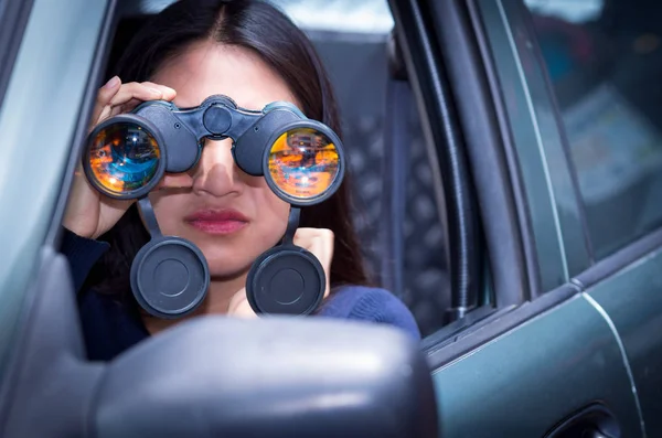 Mujer joven acechando con unos prismáticos negros dentro de su coche —  Fotos de Stock