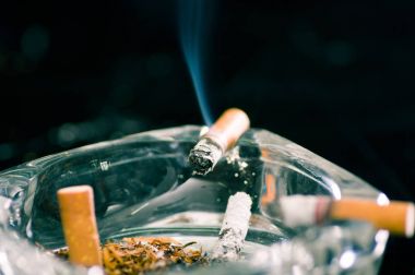 Kristal kül tablası siyah arka plan üzerinde tüketilen sigara yakın çekim