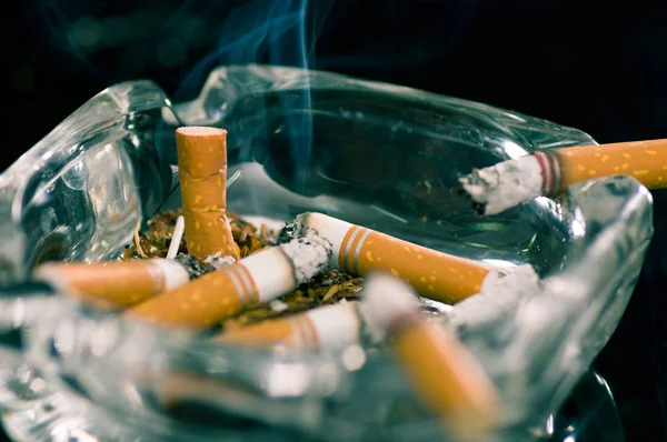 Close up de cigarros consumidos sobre um cinzeiro de cristal em fundo preto — Fotografia de Stock