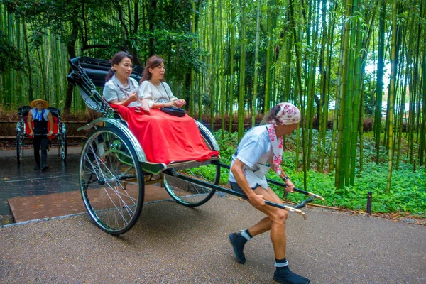 KYOTO, JAPÓN - 05 DE JULIO DE 2017: Personas no identificadas en un rickshaw rojo con una persona conduciéndolo en un camino en el hermoso bosque de bambú en Arashiyama, Kyoto, Japón —  Fotos de Stock