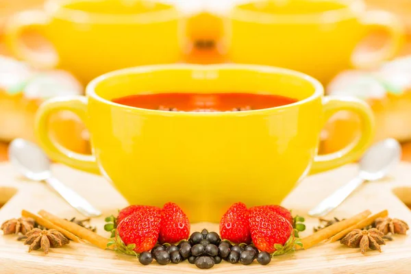 Café expresso dans une tasse jaune, avec un fruit à la fraise, raisins et cannelle devant, en fond blanc — Photo
