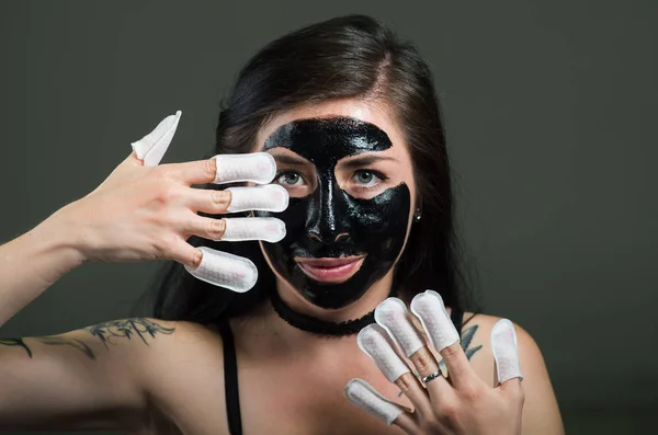 Close up of a beauty young woman using a black face mask and wearing nails protector in her nails, in a black background — Stock Photo, Image