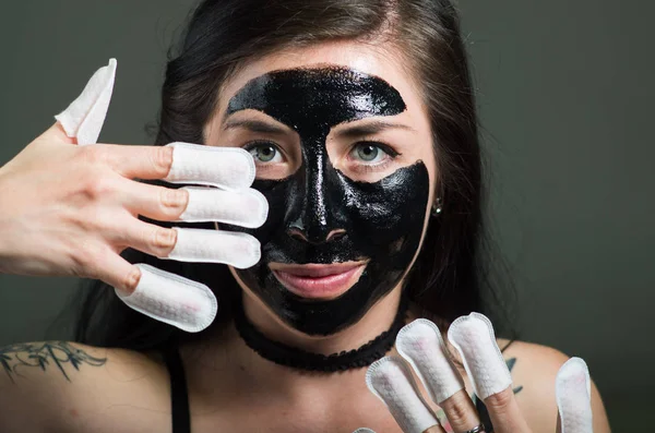 Close up of a beauty young woman using a black face mask and wearing nails protector in her nails, in a black background — Stock Photo, Image