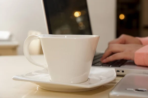 Närbild av en vit kopp kaffe med en suddig affärskvinna hand arbetar i bakgrunden. Affärsidé — Stockfoto