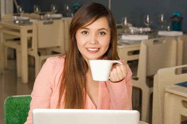 Primer plano de una joven hermosa mujer de negocios sonriente trabajando y sosteniendo con una mano una taza de café. Concepto empresarial —  Fotos de Stock