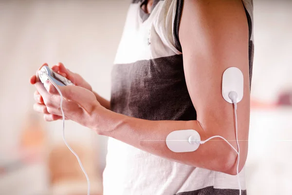 Närbild av en man som håller en elektrod maskin i handen och med electrostimulator elektroder i armen av en fitness ung man i en suddig bakgrund — Stockfoto