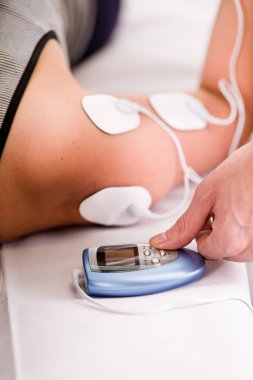 Tek eliyle bir deportist Omuzundan electrostimulator elektrotlar elektrik makineyle baş aşağı bir yatağa tutan bir kişisel antrenör Close-Up