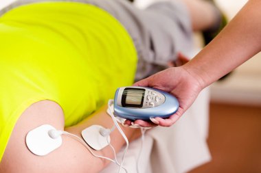 Baş aşağı bir yatak üzerinde yeşil bir t-shirt floresan giyen bir deportist kol electrostimulator elektrotlar ile elektrik makine tek eliyle tutarak kişisel bir eğitmen Close-Up