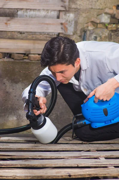 Bonito faz-tudo segurando em sua mão o spray de pintura, pintura trabalhador da construção com pistola de pulverização uma estrutura de madeira ao ar livre — Fotografia de Stock