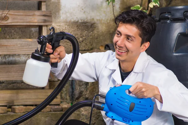 Bonito sorrindo faz-tudo segurando em sua mão o spray de pintura, pintura trabalhador da construção civil com pistola de pulverização uma estrutura de madeira ao ar livre — Fotografia de Stock