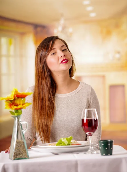 Porträtt av vacker elegant kvinna med långt hår med mat och rödvin över tabellen i en restaurang. Ung kvinna äta ensam på en restaurang i suddig bakgrund — Stockfoto