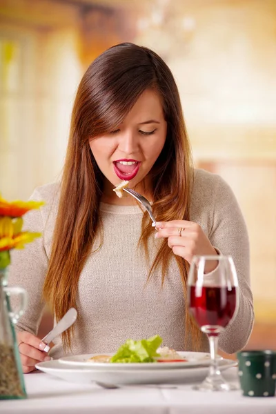 Porträtt av vacker elegant kvinna med långt hår med mat och rödvin över tabellen i en restaurang. Ung kvinna äta ensam på en restaurang i suddig bakgrund — Stockfoto